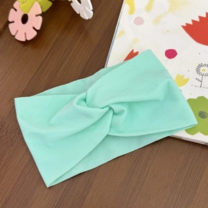 Detail view of a soft mint green knotted baby headband on a rustic wooden background