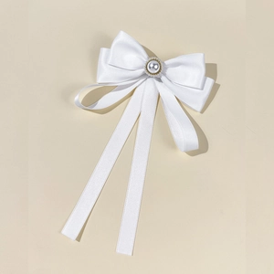 Macro shot of white satin bow brooch with large pearl center and flowing ribbons