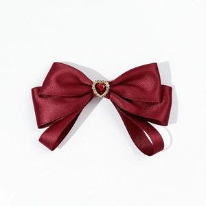 Macro detail of burgundy satin bow tie featuring a heart-shaped ruby gemstone and crystals