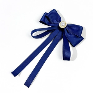 Detail view of navy blue ribbon bow with a large pearl and golden accents on a white base