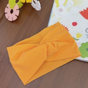 Detail of soft bright orange knotted elastic headband for baby on a wooden background