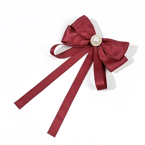 Close-up of wine red satin bow with elegant faux pearl center and long ribbon streamers