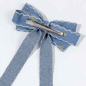 Detail of light blue denim bow hair clip with star studs and silver metal duckbill clip
