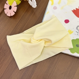 Detail view of cream twist knot baby headband on a wooden table with kids toys