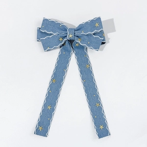 Detail view of denim bow hair clip with white wavy embroidery and gold stars
