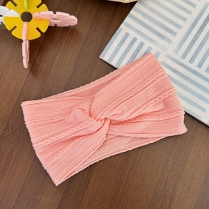 Detail of soft pink cable-knit baby headband with twisted knot on wooden background