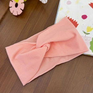 Detail of baby pink knotted headband made of soft elastic knit fabric on a wooden desk