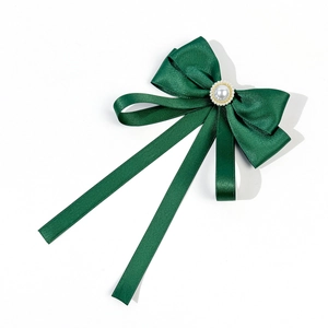 Close-up of dark green satin ribbon bow brooch with elegant pearl and gold trim detail