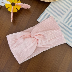 Detailed view of pink knitted twist baby headband with cable texture on wood surface