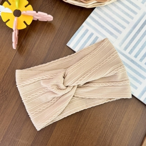 Detailed view of beige cable-knit baby headband featuring a twisted knot and elastic texture