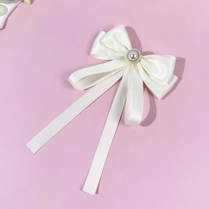 Detail of elegant cream satin bow with center pearl and gold beads on pink background