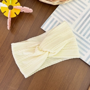 Close-up of cream knitted baby headband with soft cable twist texture on wood background