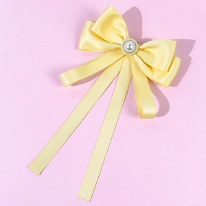 Detail of yellow satin bow tie with central pearl and rhinestones on pink background