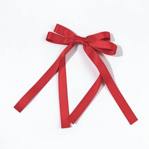 Detail of red ballet bow hair clip showing textured ribbon fabric and long hanging streamers