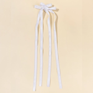 Dettaglio di un fermaglio per capelli a fiocco bianco con bordi in pizzo e nappe lunghe