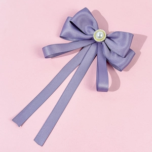 Detail of purple satin bow brooch with large faux pearl and golden trim on pink background