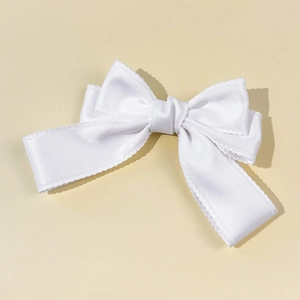Détail de la pince à cheveux en satin blanc avec bords festonnés et texture soyeuse