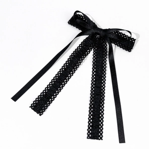 Détail d'un nœud à cheveux en dentelle noire avec rubans texturés et pompons à franges