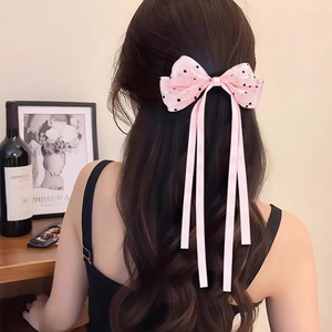 Gros plan d'une pince à cheveux nœud rose à pois avec longs rubans sur cheveux bouclés
