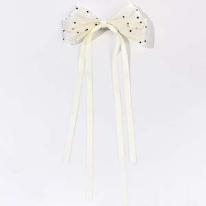 Détail de la pince à cheveux noeud beige à pois noirs avec de longs rubans fluides élégants