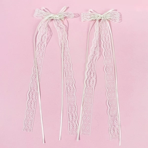 Paire de barrettes en dentelle beige avec longs rubans élégants sur fond rose pastel