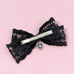 Elegant black lace bow hair clip with a silver heart pendant on a pink background