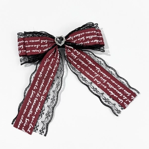 Close-up of burgundy bow hair clip with black lace, heart gemstone, and script patterns