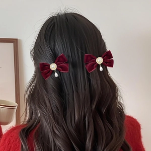 Detail of wine red velvet bow hair clips with pearls on elegant wavy dark hair