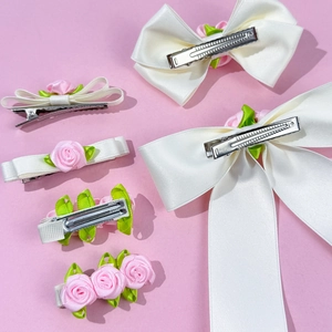 Set de barrettes avec fleurs roses et nœuds en satin blanc sur fond pastel rose