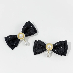 Detalle de los clips de lazo negro con perlas y tachuelas en patrón de espiga