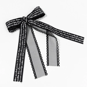 Detail of black ribbon bow with white cursive text and delicate wavy lace edges