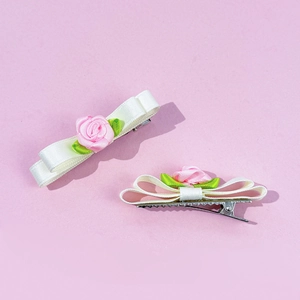 Détail de barrettes à cheveux avec nœud en satin blanc, rose rose et petites feuilles
