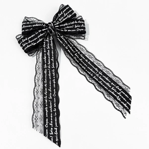 Detail of black lace bow hair clip with white cursive text and intricate wave edges