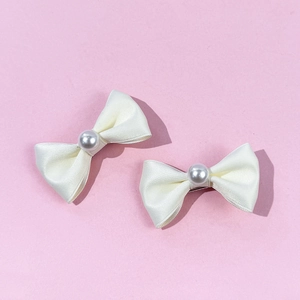 Détail de barrettes nœuds en satin crème avec perles sur un fond rose poudré