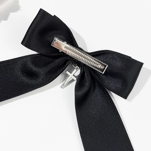 Close-up of black satin bow hair clip with silver cross pendant and metal duckbill clip