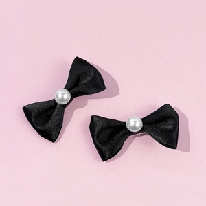 Détail de barrettes nœuds en satin noir avec perle centrale sur fond rose tendre