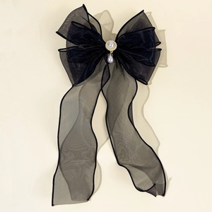 Detail of black mesh bow hair clip featuring central pearl and sparkling rhinestones