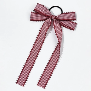 Detail view of a plaid fabric bow hair tie with red and white patterns and long tails