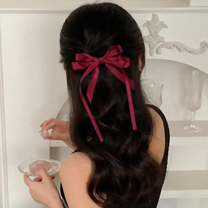 Close-up of wine red silk bow hair clip on long wavy hair with elegant ribbon tails