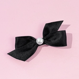 Détail d'une pince à cheveux avec nœud en satin noir et une perle blanche au centre