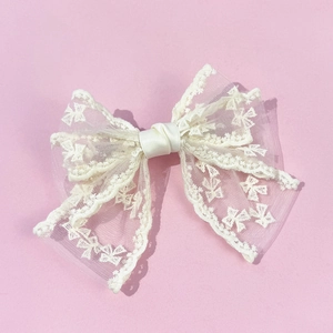 Close-up of cream lace bow hair clip featuring intricate wavy embroidery and mesh texture