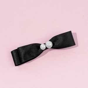 Détail d'une barrette à cheveux nœud noir avec perles brillantes sur fond rose doux