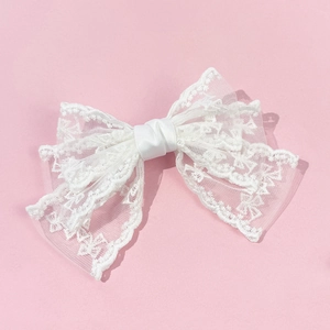 Detail of white lace bow hair clip with intricate scalloped edges and ribbon center