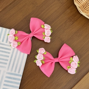 Close-up of pink ribbon bow hair clips with delicate silk roses and green leaf details