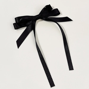 Detail of a thin black headband with serrated edges and a glossy satin ribbon bow