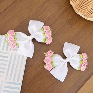 Sweet floral bow hair clips with pink fabric flowers and green leaves on wooden background