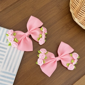 Detailed macro view of two pink satin bow hair clips with rose and leaf accents
