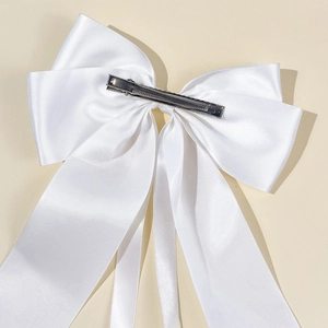 Detail of white satin bow hair clip featuring an elegant long ribbon and metal spring clip