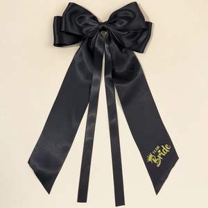 Detailed view of black satin bow hairclip with gold TEAM Bride crown print and long streamers