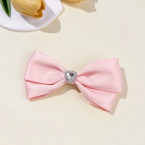 Detail of pink bow hair clip with a sparkling heart-shaped crystal on a beige background